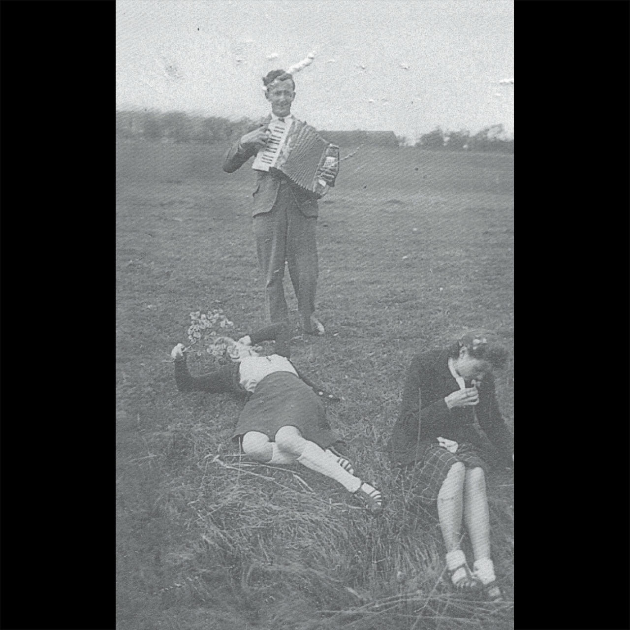 an acordeonist and two girls in a field in the 50s